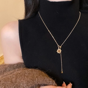 Detail of tiger eye sun pendant on Y-shaped golden necklace worn with black sweater