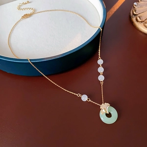 Detail of gold ginkgo leaf and green jade pendant necklace on an elegant dark wood surface