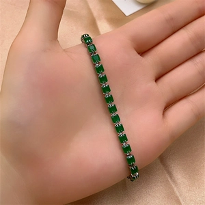 Detail of silver bracelet with rectangular emerald green zircons on silk background