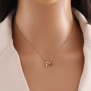 Détail du pendentif lettre F dorée avec perle œil bleu sur une chaîne de collier fine