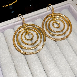 Detailed close-up of golden multi-layered circular drop earrings on a grey velvet base