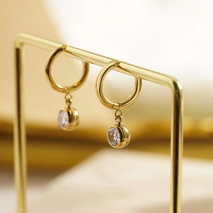 Elegant gold titanium steel hoop earrings with round crystal charms on a display stand