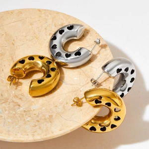 Polished gold and silver C-shaped hoop earrings with hollow heart patterns on marble plate