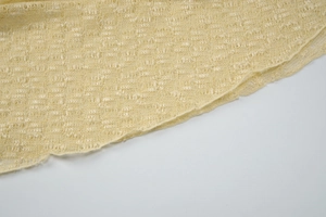 Close-up of yellow French lace knit fabric showing intricate hollow floral patterns