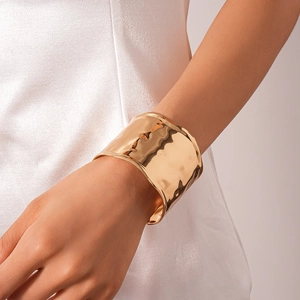 Detail of a wide gold open cuff bracelet with hammered texture on a model's wrist