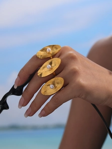 Detailed view of large gold oval ripple rings with pearls on model's hand at the beach
