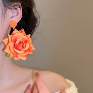 Detail of elegant orange fabric rose earrings worn by a model in a side profile view