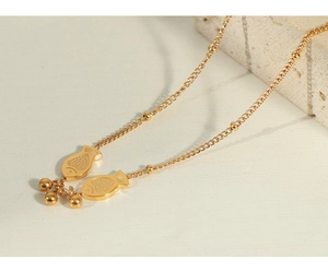 Detailed close-up of golden fish pendant and beaded chain on a white stone surface