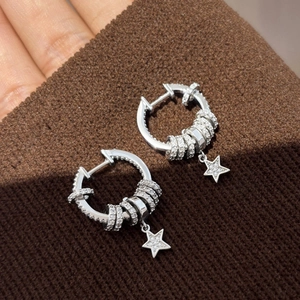 Macro detail of silver star drop earrings with white zircon on brown knit fabric