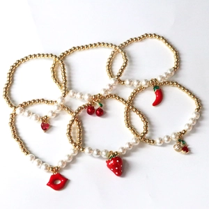 Macro detail of cherry and strawberry fruit charms on gold pearl beaded bracelets