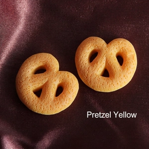 Macro view of two biscuit yellow resin pretzel charms on brown silk fabric