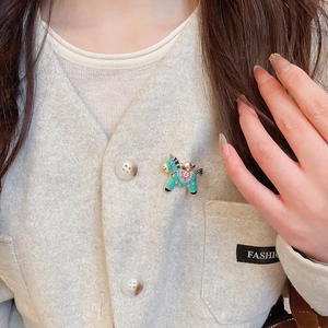 Detail of green enamel horse brooch with floral pattern on a grey wool vest
