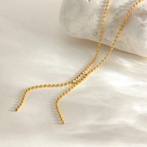 Détail du collier en Y doré avec quatre strass brillants sur une surface blanche texturée