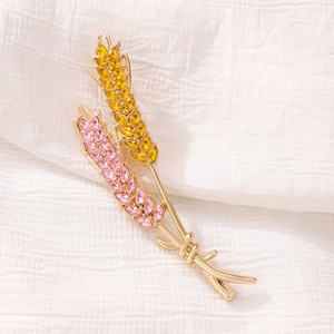Close-up of golden wheat brooch with pink and yellow crystals on white fabric