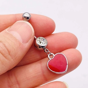 Detail of silver belly ring with a clear crystal and a vibrant red heart pendant