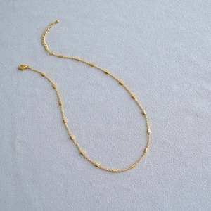 Detailed close-up of a minimalist gold-plated necklace with elegant metal tube accents