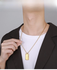 Close-up of a polished gold dog tag necklace worn over a dark suit and white t-shirt