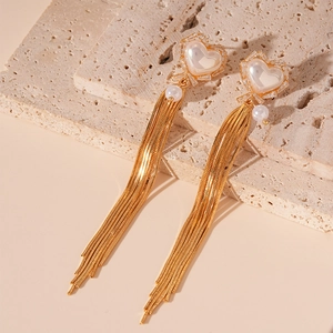 Detail of golden heart earrings with long metal tassels and pearls on a warm stone base
