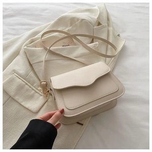Detail of cream faux leather crossbody bag with adjustable strap on beige blazer