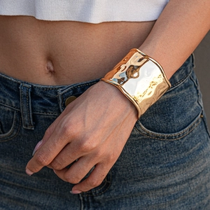 Detailed close-up of golden wide open cuff bracelet with hammered metallic texture