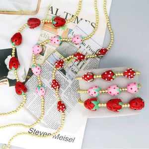 Detailed shot of red and pink strawberry beaded necklace set with gold accents on newspaper