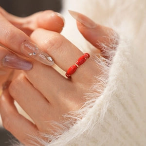 Detail of red enamel oval ring on model with golden ring links and plush white knitwear