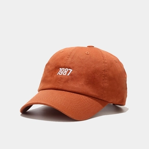 Detailed embroidery of 1987 on burnt orange cotton canvas baseball cap surface