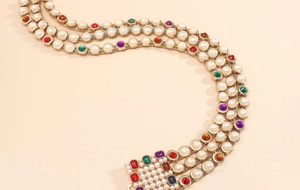 Detail of multilayered gold chain belt featuring colorful rhinestones and elegant white pearls