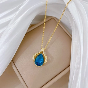 Detail of blue teardrop pendant with gold setting on a soft white silk background