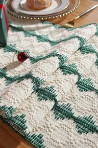 Detail of green and white geometric knit table runner with tassels on a wooden surface
