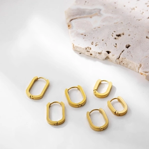 Macro detail of three pairs of minimalist 18K gold rectangular hoop earrings on white stone
