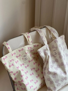 Deux sacs fourre-tout en toile avec nœuds roses et violets posés sur une chaise blanche