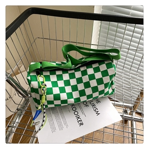 Green checkerboard canvas barrel bag with woven strap detail inside a metal cart