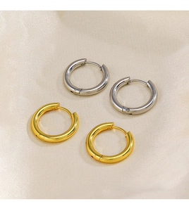 Detailed view of polished 18K gold and silver hoop earrings on beige silk fabric
