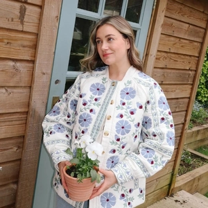 Outdoor shot of a white quilted floral jacket with detailed blue and red embroidery