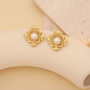 Elegant gold flower shell earrings with central white pearls on minimalist stone backdrop