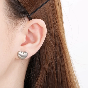Gros plan de boucles d'oreilles cœur minimalistes brossées sur mannequin au fini mat élégant