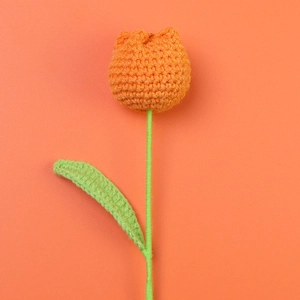 Close-up of handmade crochet tulip flower with orange petals and green stem detail