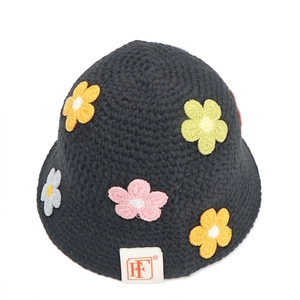 Detail of hand-knitted black bucket hat with colorful floral crochet and white brand tag