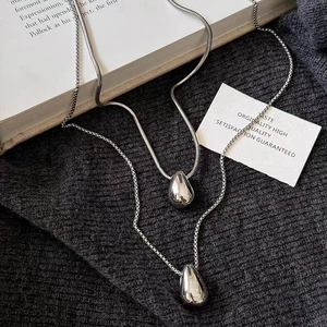 Minimalist silver water drop pendant necklace set on a dark grey knitted sweater background