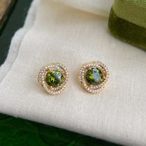 Macro shot of gold stud earrings featuring olive green gemstones and white zircon halo