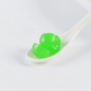 Macro shot of realistic green PVC mini apples on a ceramic spoon for DIY cake decoration