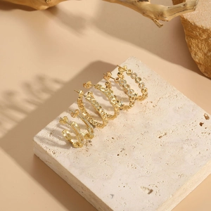 Detailed shot of 14K gold plated zircon earrings displayed on a beige stone slab