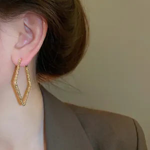 Irregular geometric gold hoop earrings with textured finish on female model