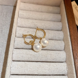 Détail macro de créoles dorées avec perles blanches présentées dans un écrin à bijoux