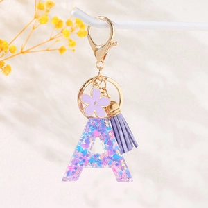 Detail of purple sequin letter A keychain with tassel and floral charm in golden finish