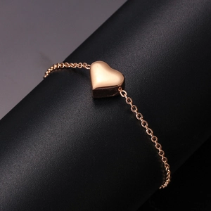 Macro view of polished rose gold heart charm on a minimalist stainless steel link bracelet