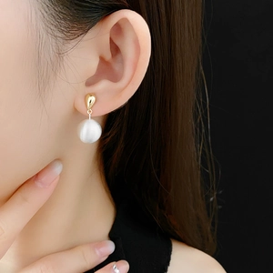 Détail d'une boucle d'oreille goutte dorée avec une grande perle blanche sur modèle
