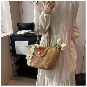 Detail of straw woven tote with brown leather flap, pearl buckle, and lace ribbon accent