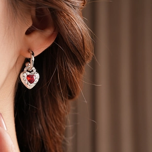 Detailed close-up of a silver heart earrings with a central red gemstone on a model